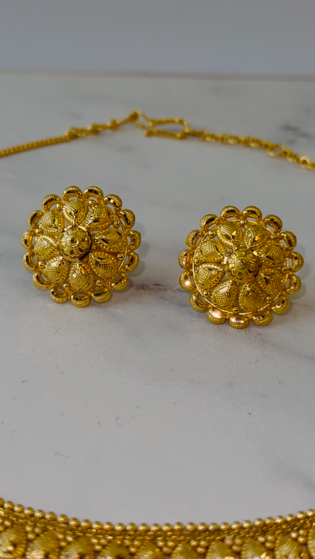 Gold necklace and earrings on a white marble surface