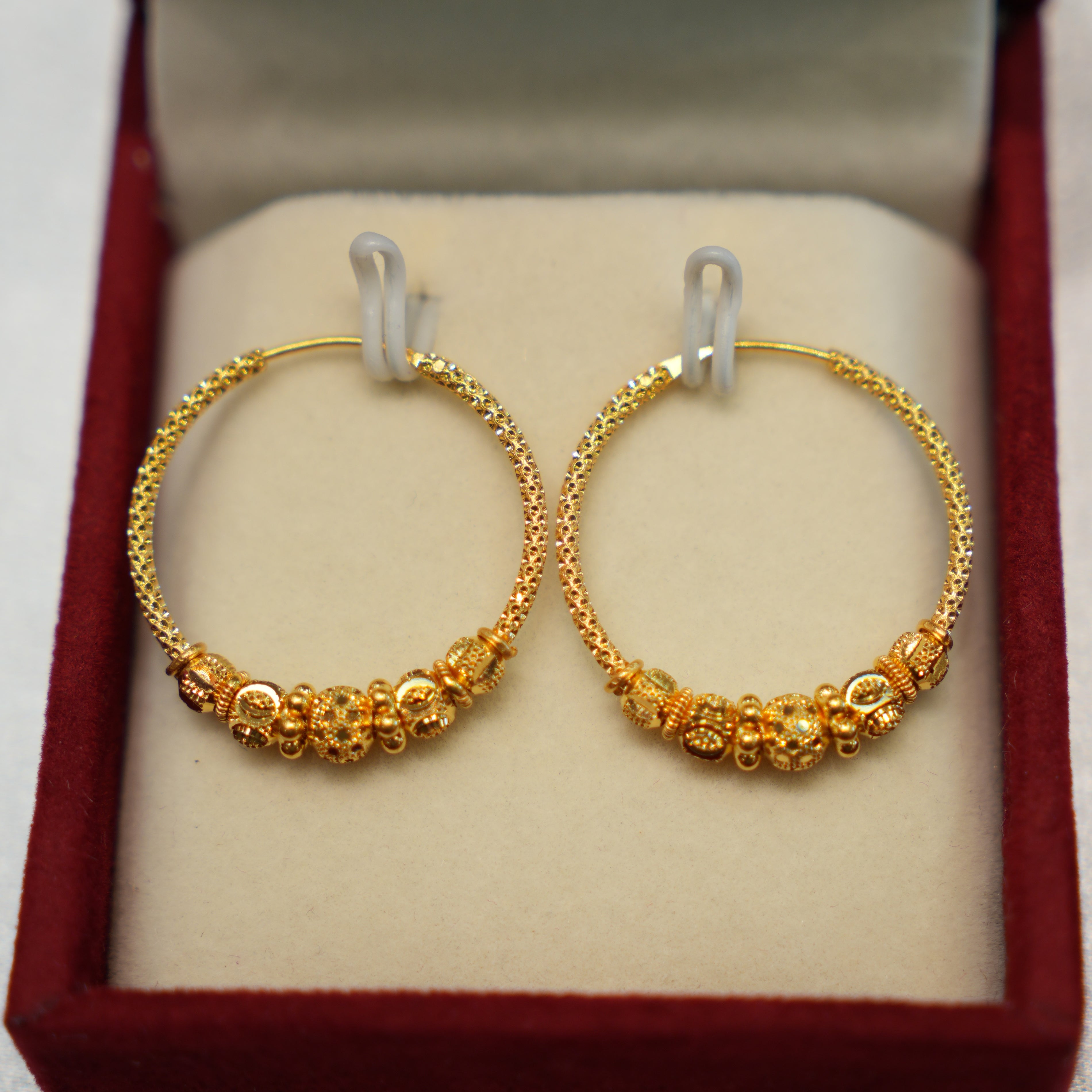 Gold hoop earrings with intricate designs in a red box.