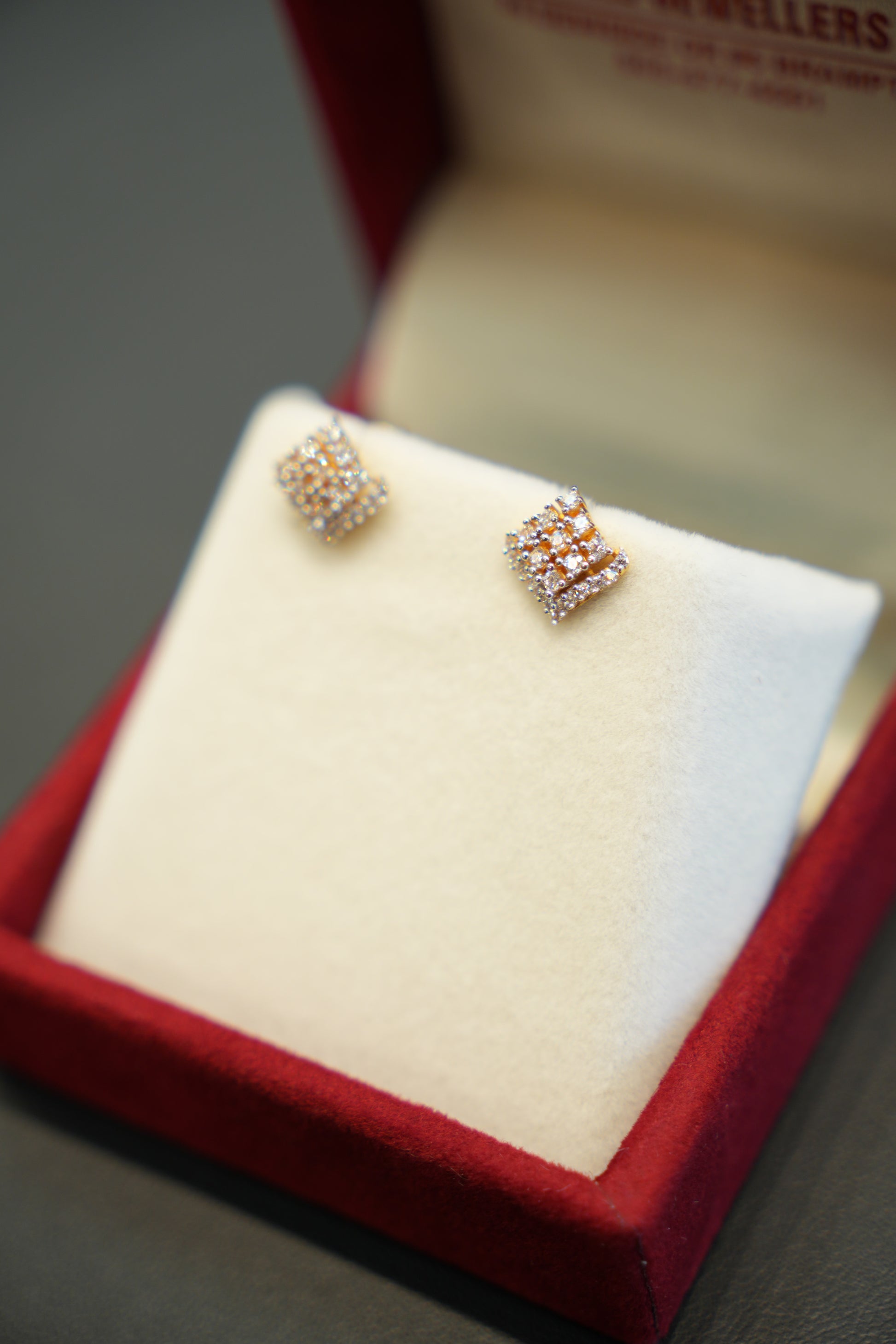 Pair of diamond earrings on a white cushion in a red jewelry box.