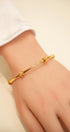 Gold bracelet on a person's wrist with a plain background