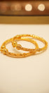 Two gold bracelets on a beige surface with a blurred background