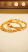 Two gold bracelets on a beige surface with a blurred background
