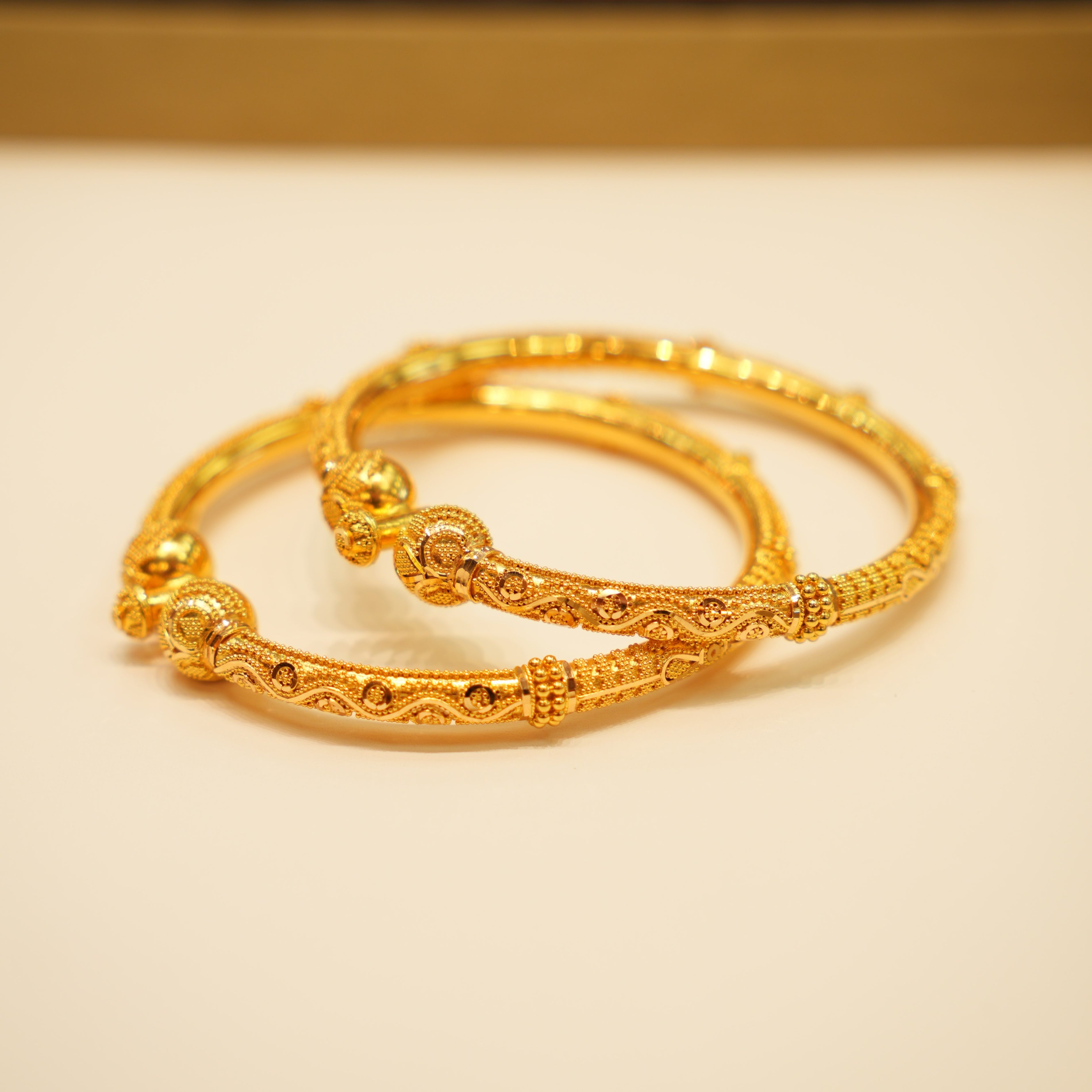 Two gold bracelets on a beige surface with a blurred background