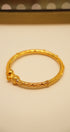 Gold bracelet on a beige surface with a polka dot pattern in the background