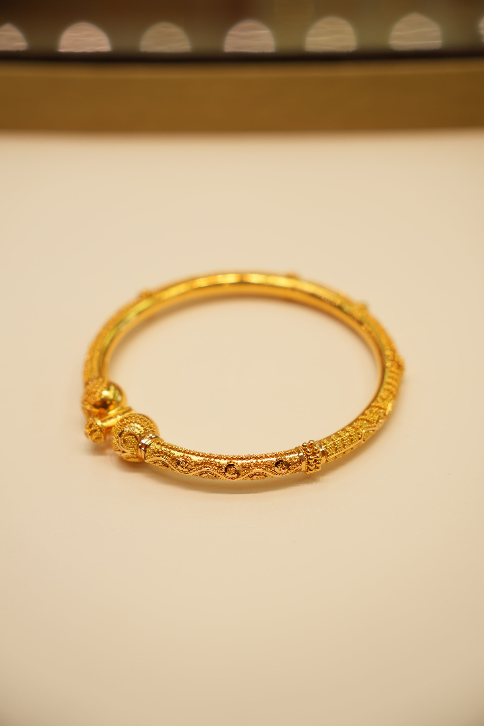 Gold bracelet on a beige surface with a polka dot pattern in the background