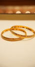 Two gold bangles on a beige surface with a blurred background