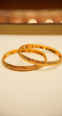 Two gold bangles on a beige surface with a blurred background