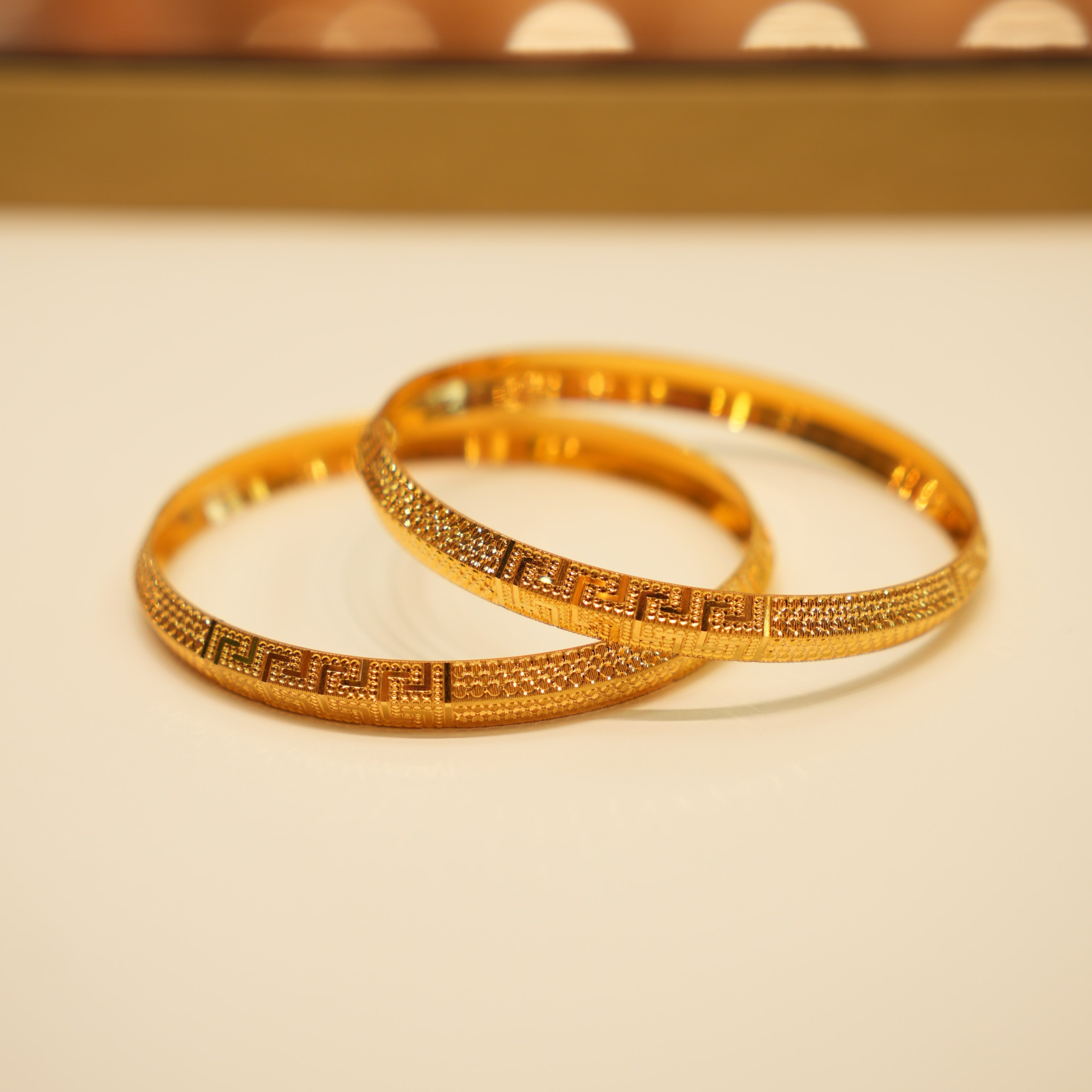 Two gold bangles on a beige surface with a blurred background