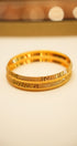 Gold bracelet with intricate design on a beige background