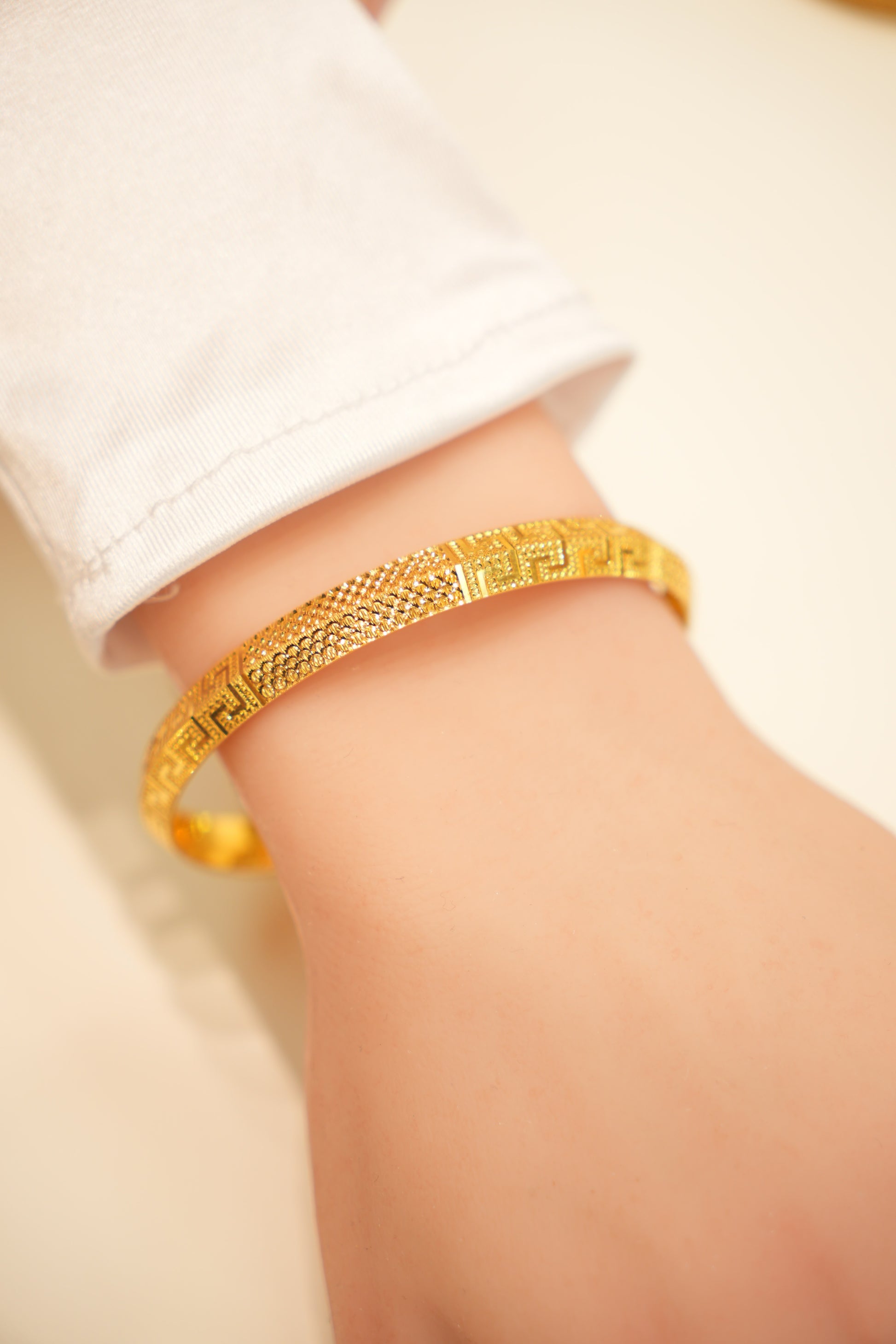 Gold bracelet on a person's wrist with a plain background
