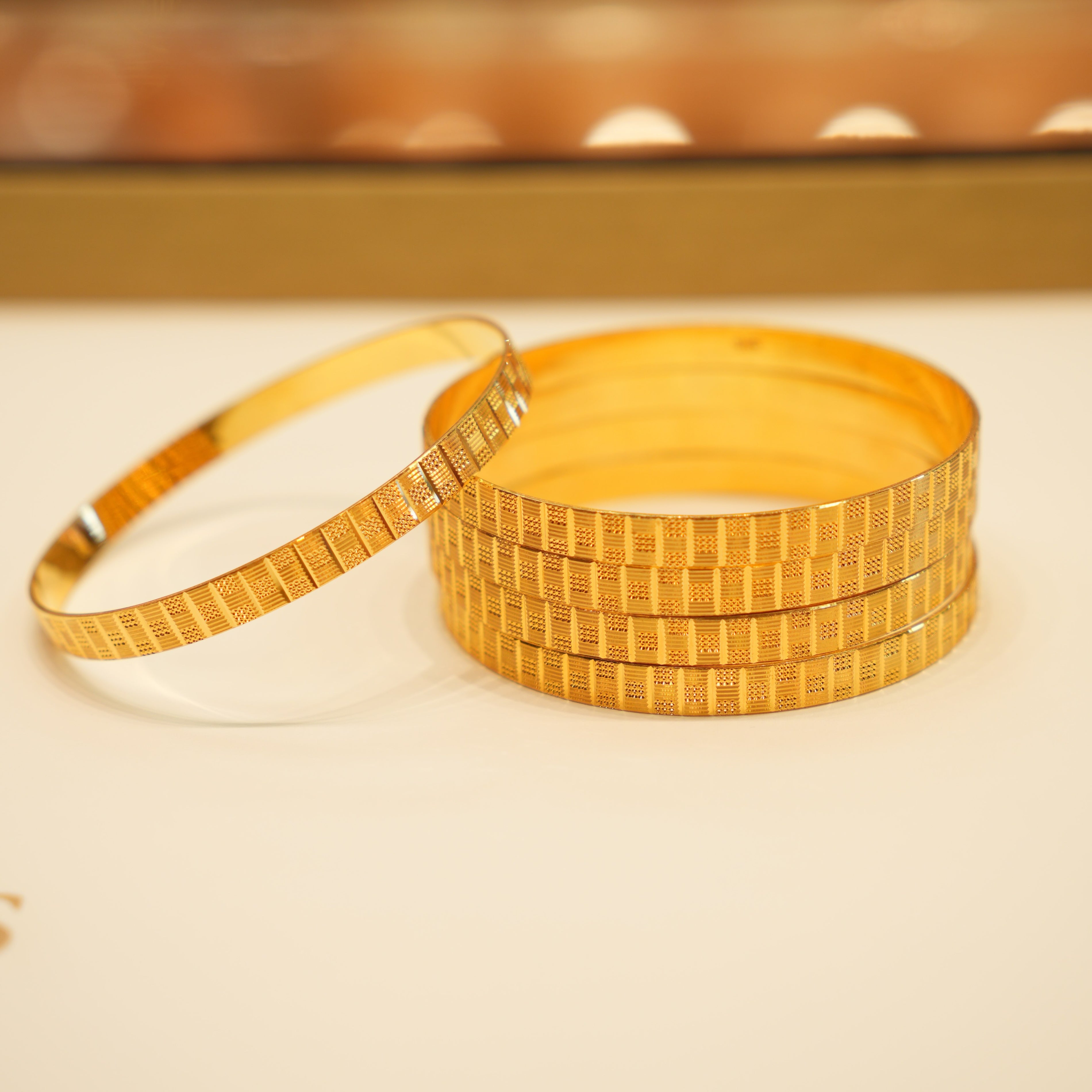Stack of gold bangles on a beige surface with a blurred background