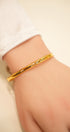 Gold bracelet on a person's wrist with a plain background