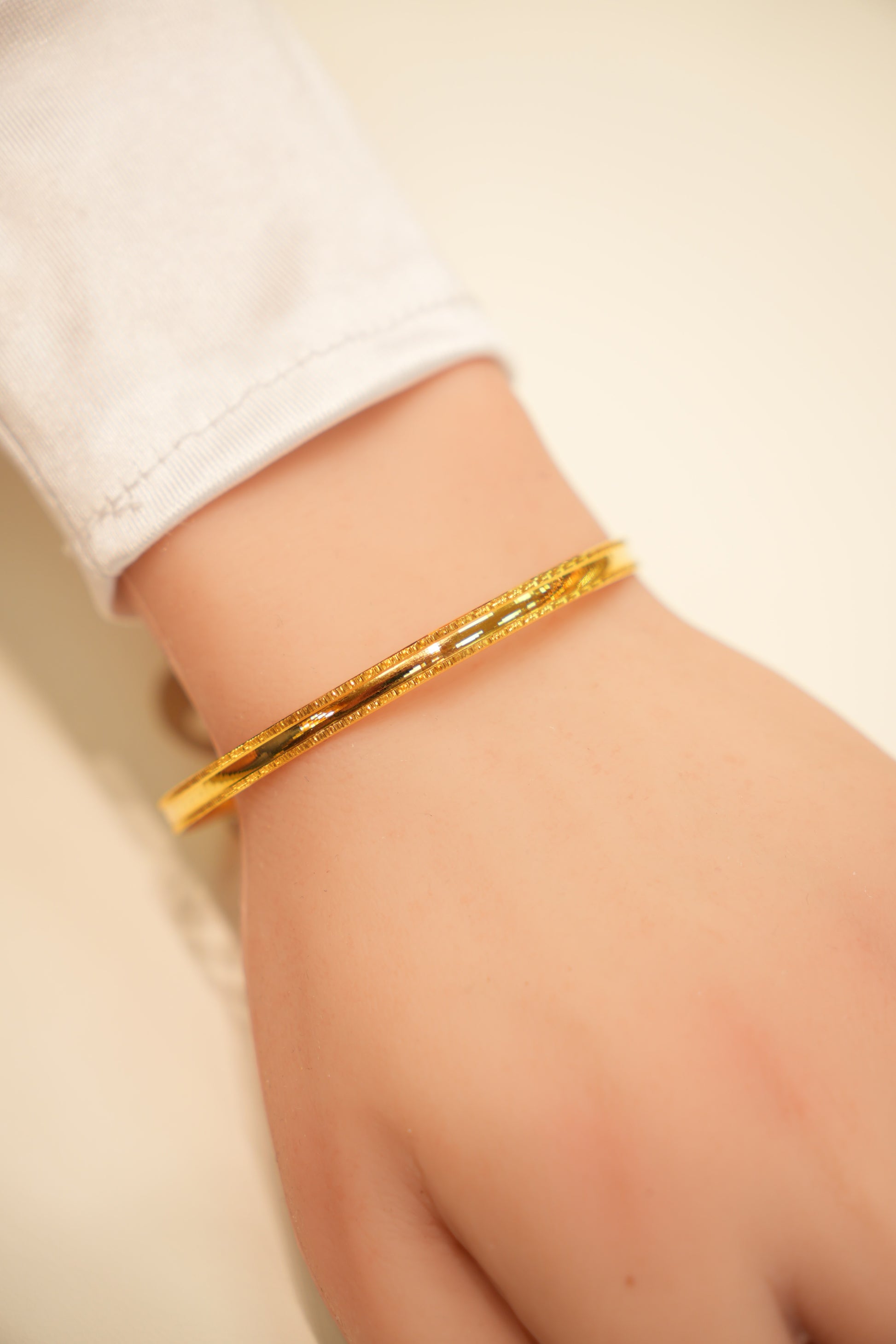Gold bracelet on a person's wrist with a plain background
