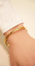 Gold bracelet on a wrist with a neutral background