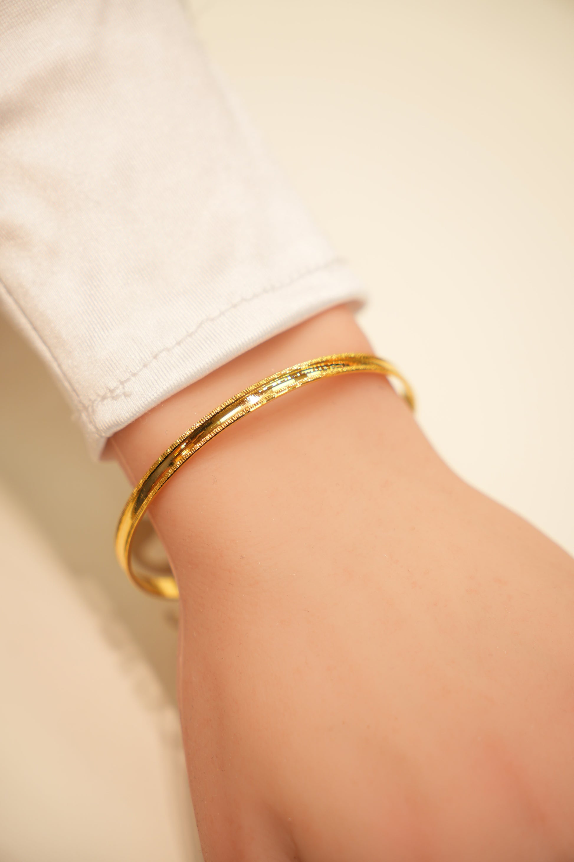 Gold bracelet on a wrist with a neutral background