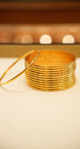 Stack of gold bangles on a white surface with a blurred background