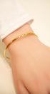 Gold bracelet on a wrist with a plain background