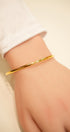 Gold bracelet on a wrist with a plain background