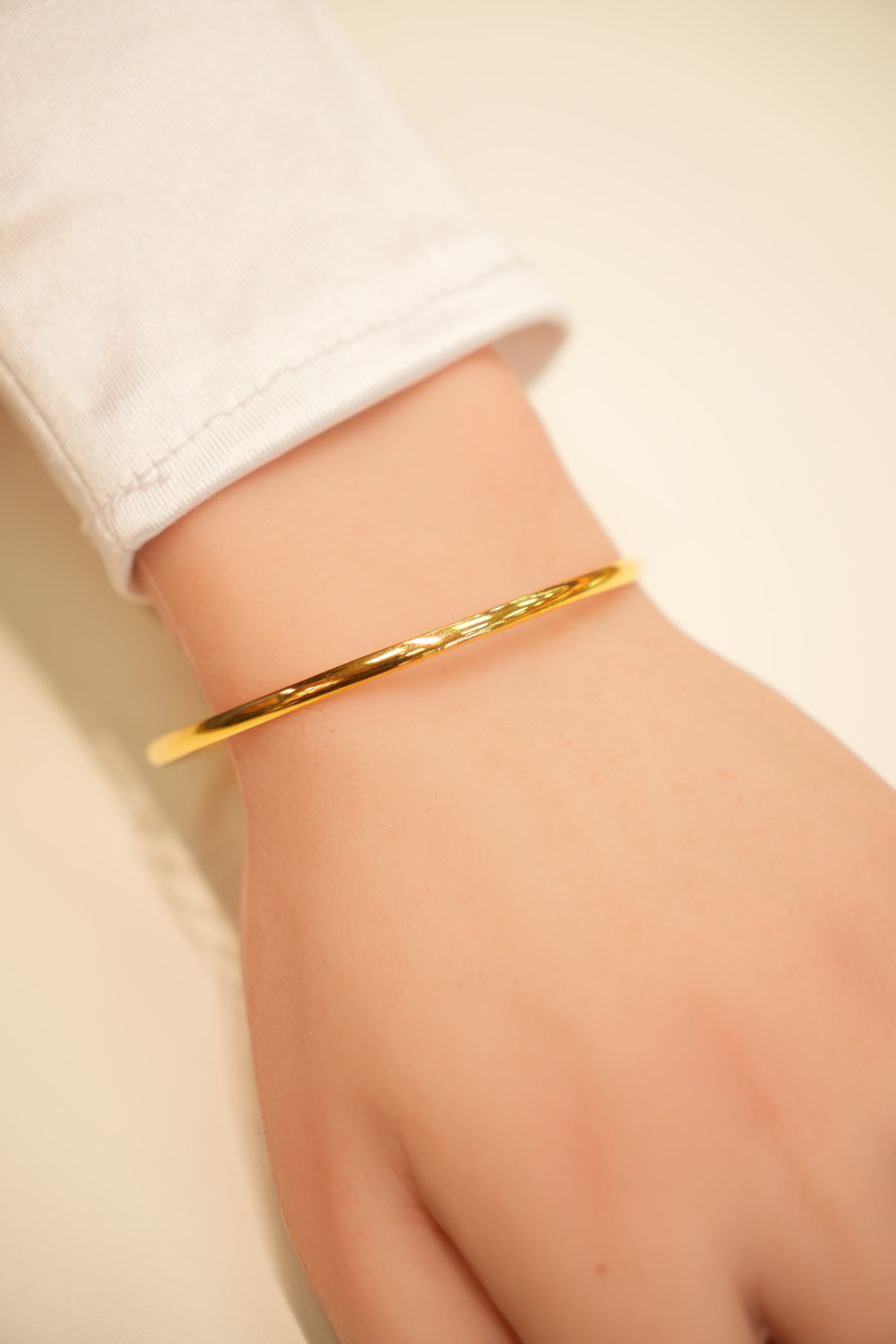 Gold bracelet on a wrist with a plain background