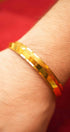 Gold bracelet on a wrist with a red background