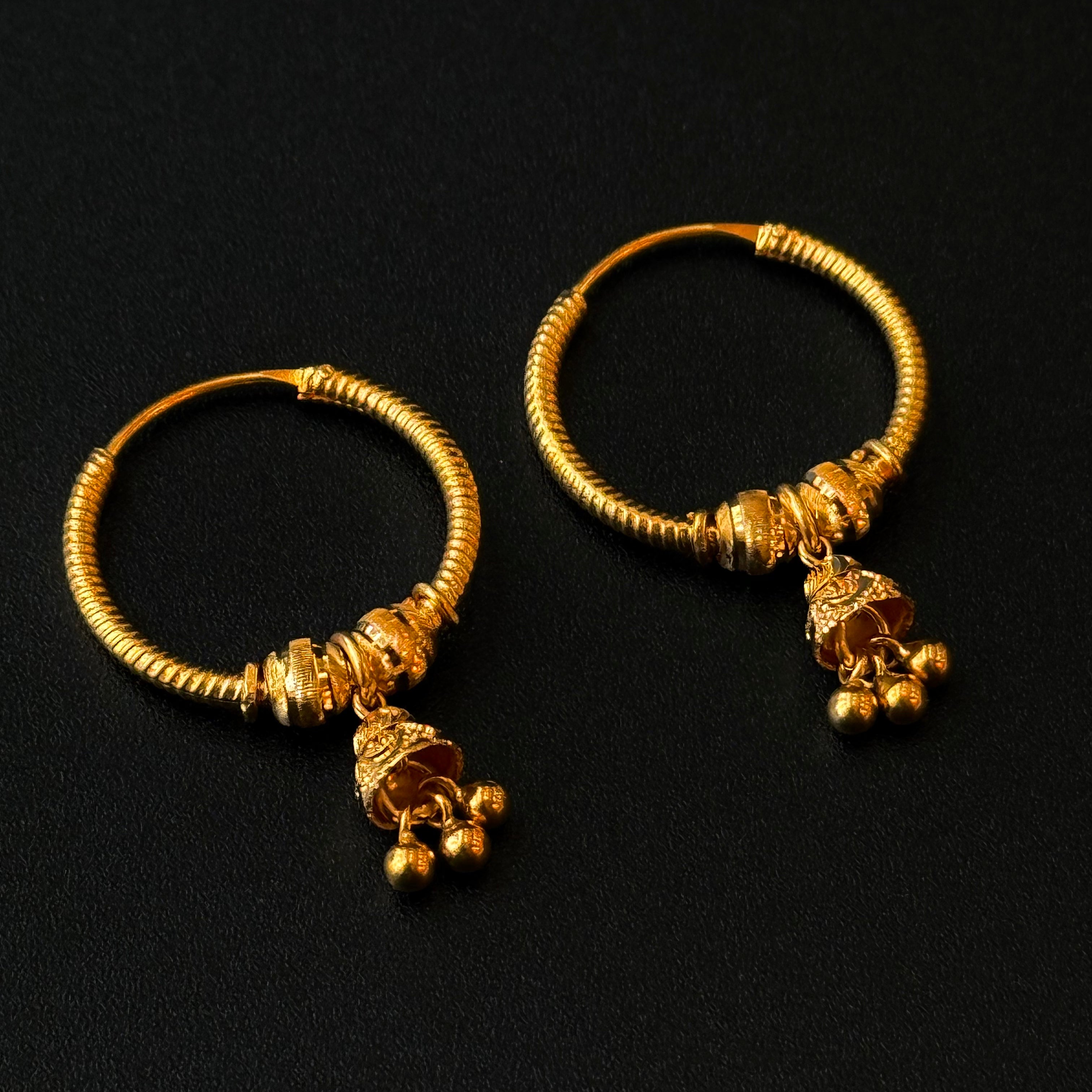 Pair of gold hoop earrings with small dangling charms on a black background
