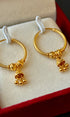 Gold hoop earrings with small charms on a red and beige jewelry box.
