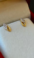 Gold earrings with gemstones on a white cushion inside a jewelry box.