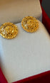 Pair of gold earrings on a white cushion with a red border