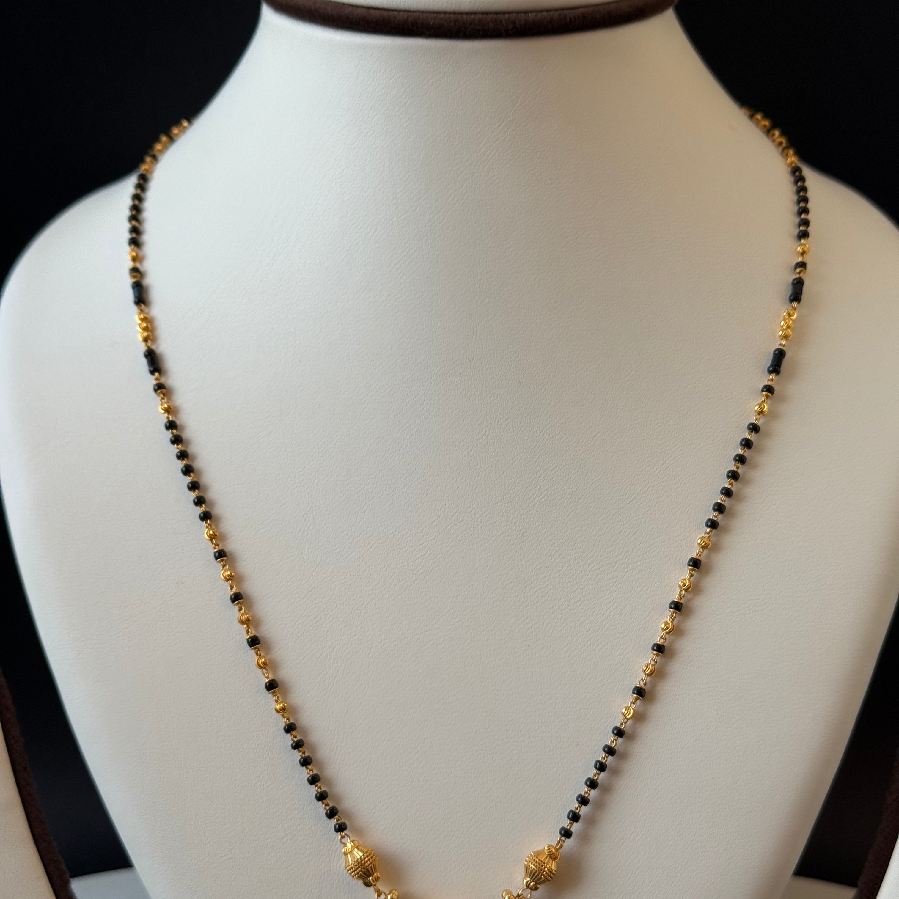 Necklace with black and gold beads on a mannequin bust against a black background